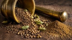 Close-up of whole cumin seeds, coriander seeds and cardamom pods spilling from a brass mortar and pestle next to a small pile of freshly ground spice