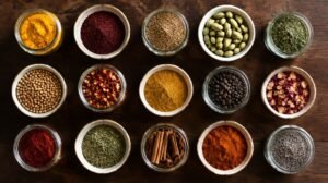 Neatly arranged collection of fifteen small glass spice jars and ceramic bowls filled with colorful Middle Eastern spices on a dark wooden table, turmeric